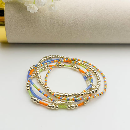 Set of colorful beaded bracelets on a white surface with a gold and beige cylindrical object in the background.