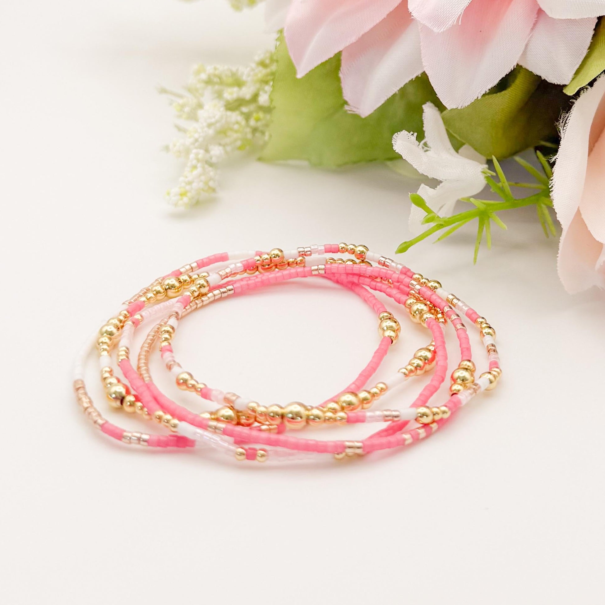 Set of pink and gold beaded bracelets with flowers on a white background